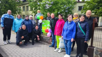 Socialinių dirbtuvių Metų ratas dalyviai, socialinė darbuotoja, meistrės stovi prie šventinio kvietimo į atvirų durų dieną